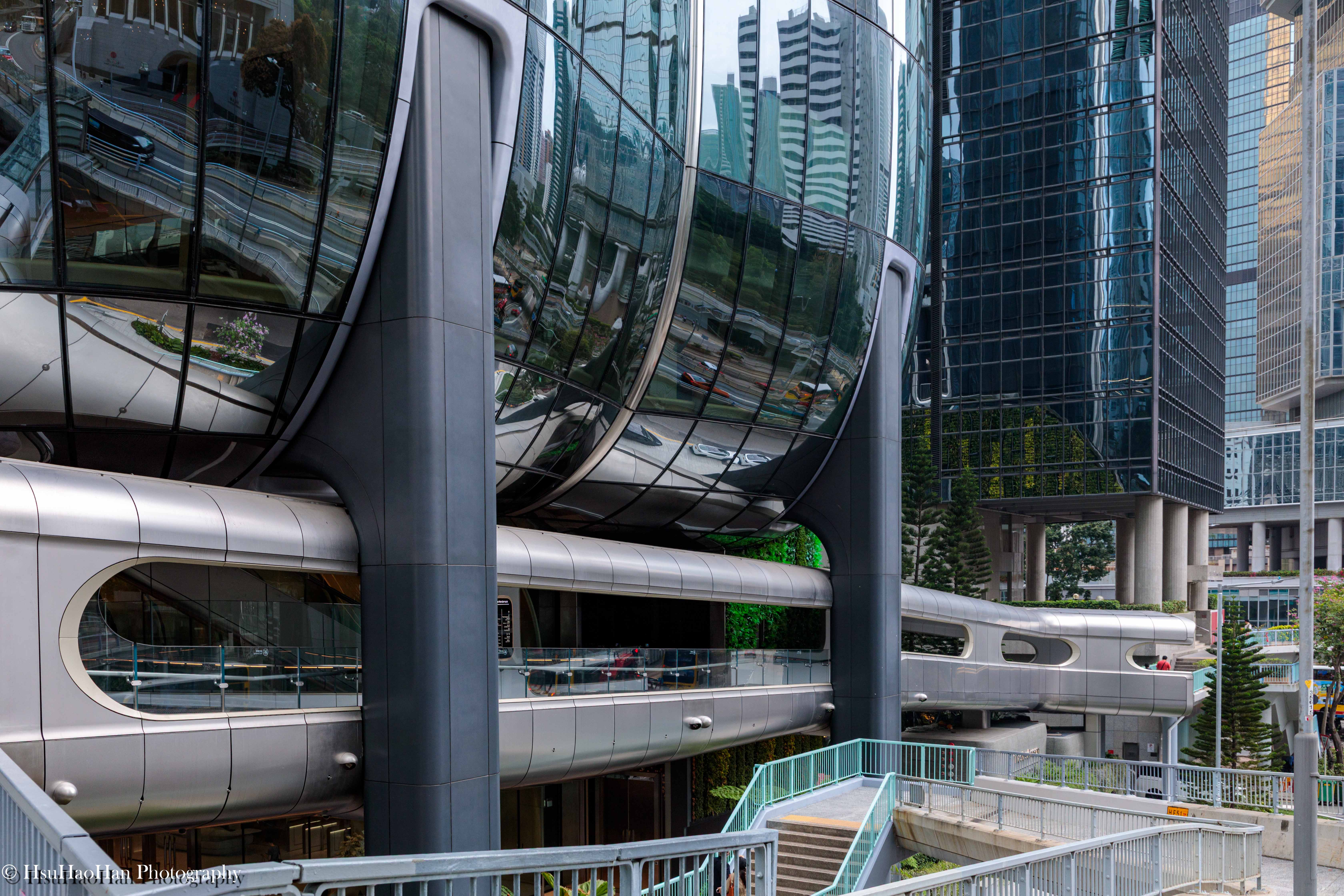 香港 The Henderson 大樓與其周圍的行人天橋系統，展現了建築有 機的曲線如何與城市的基礎設施無縫地連結。