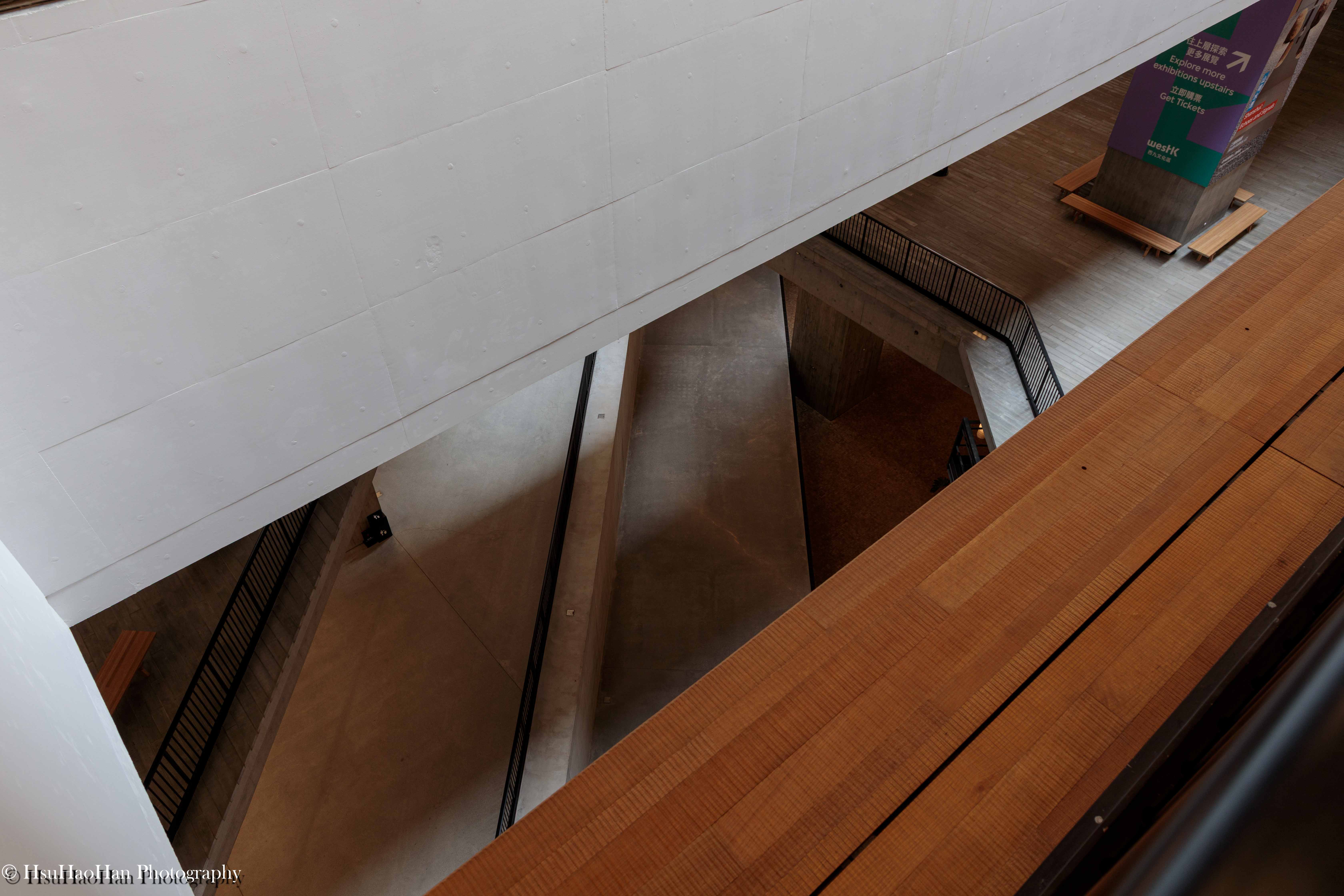 從高處俯瞰香港 M+ 博物館的內部空間，不同樓層的木質地板與清水混凝土牆面，形成抽象的幾何塊面與線條。