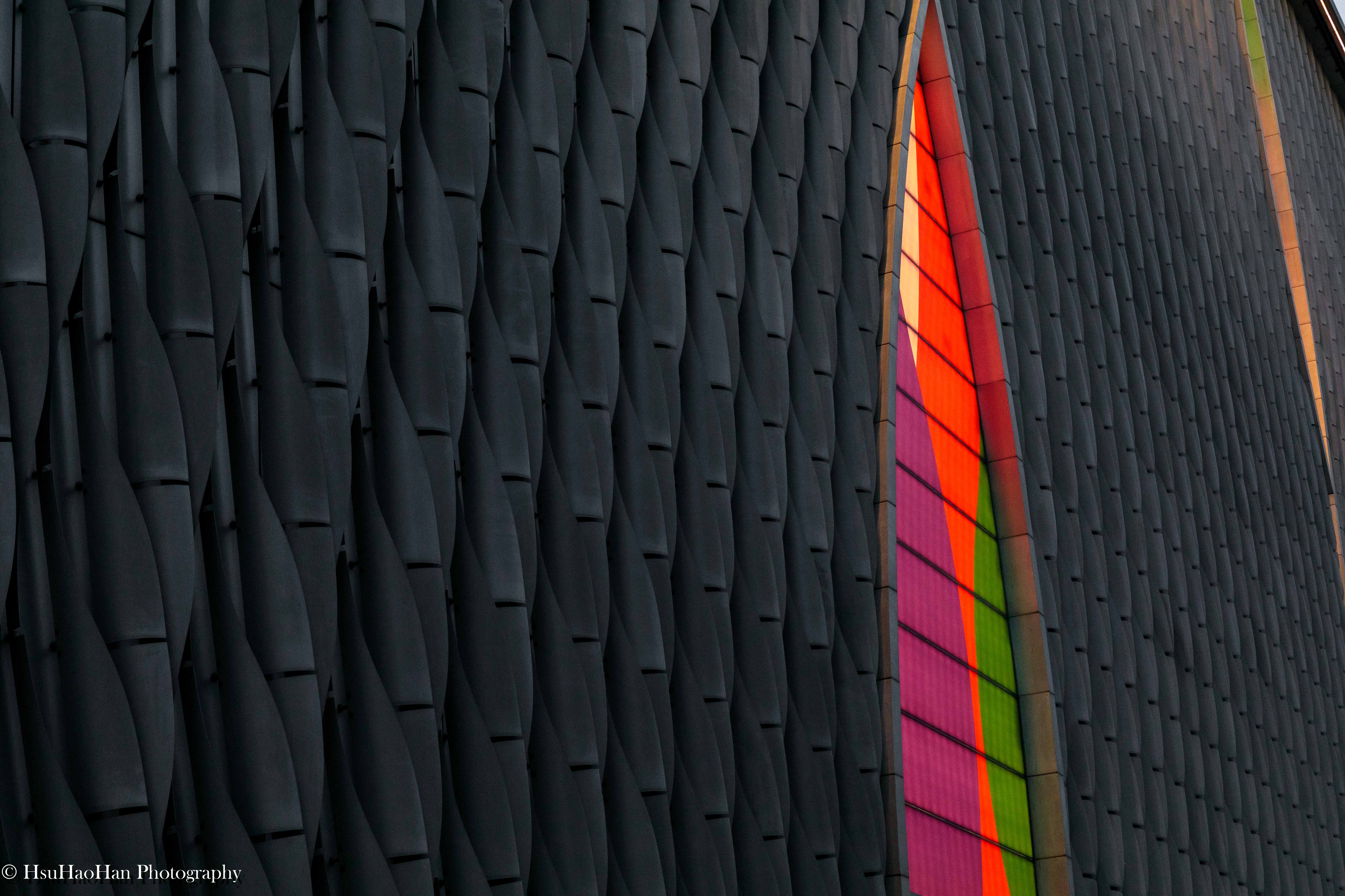 香港戲曲中心如鱗片般排列的金屬立面細節，在黃昏的餘暉下，呈現出溫暖的古銅色光澤與流動的線條。