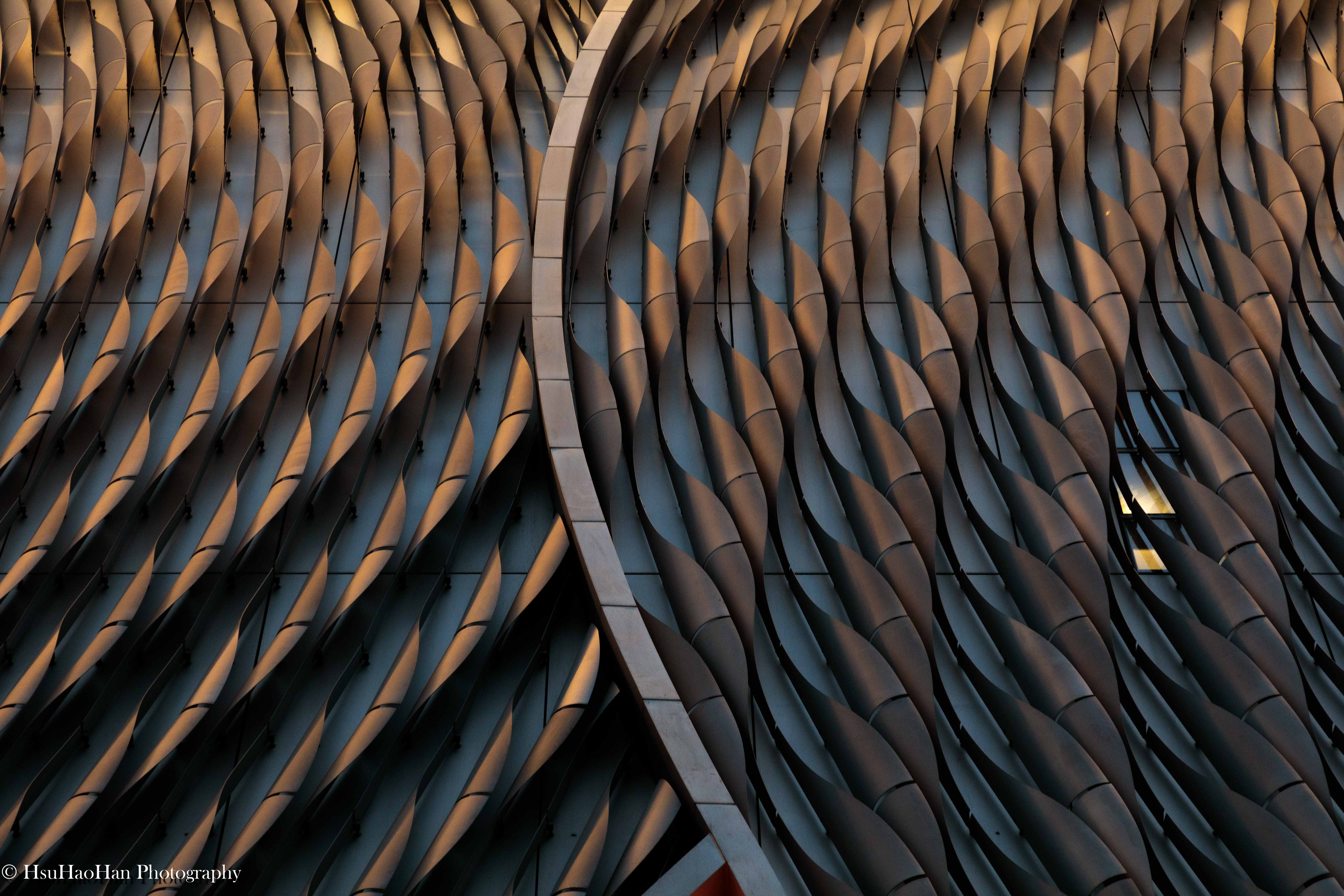香港戲曲中心如鱗片般排列的金屬立面細節，在黃昏的餘暉下，呈現出溫暖的古銅色光澤與流動的線條。