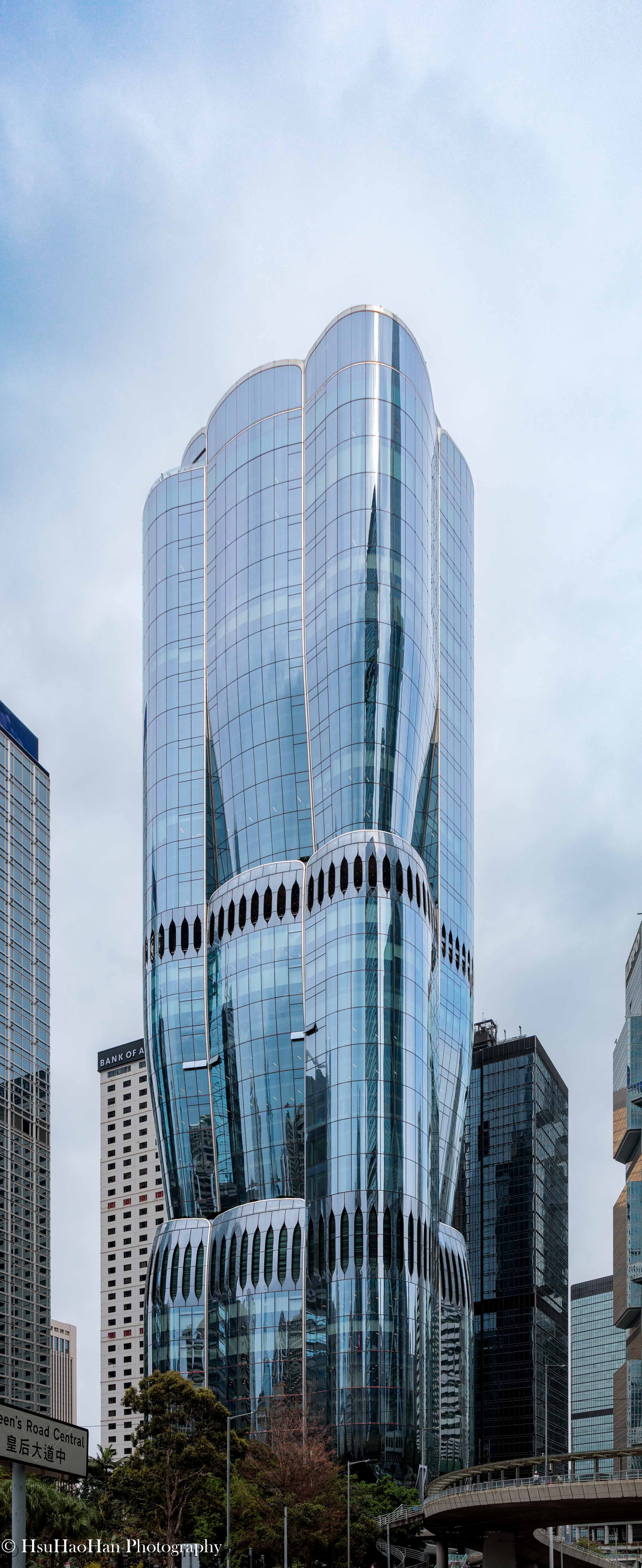 香港中環的 The Henderson 大樓正面，由 Zaha Hadid 設計，流線型的玻璃帷幕建築在陰天多雲的天空下，呈現出花蕾般的有機形態。