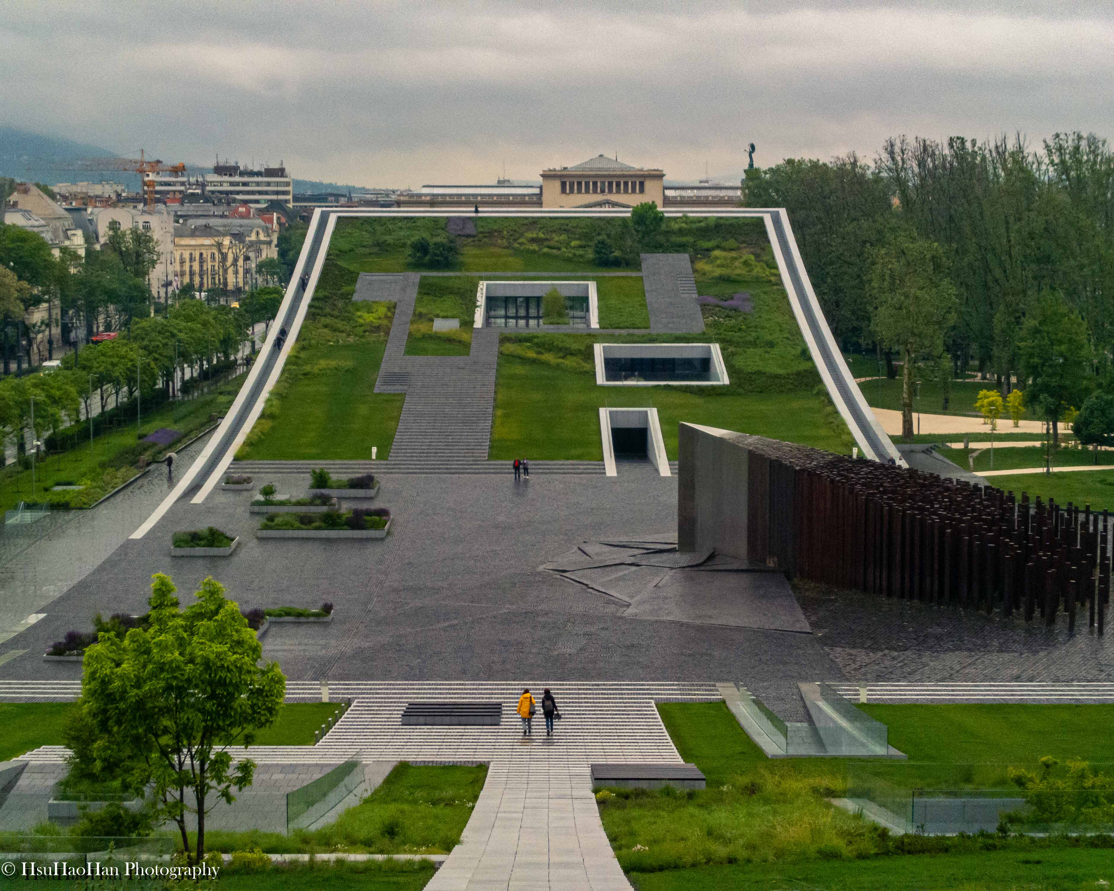從高處俯瞰匈牙利布達佩斯民族學博物館，巨大的綠色屋頂上有著幾何形狀的開口，前景是1956年革命紀念碑的廣場。