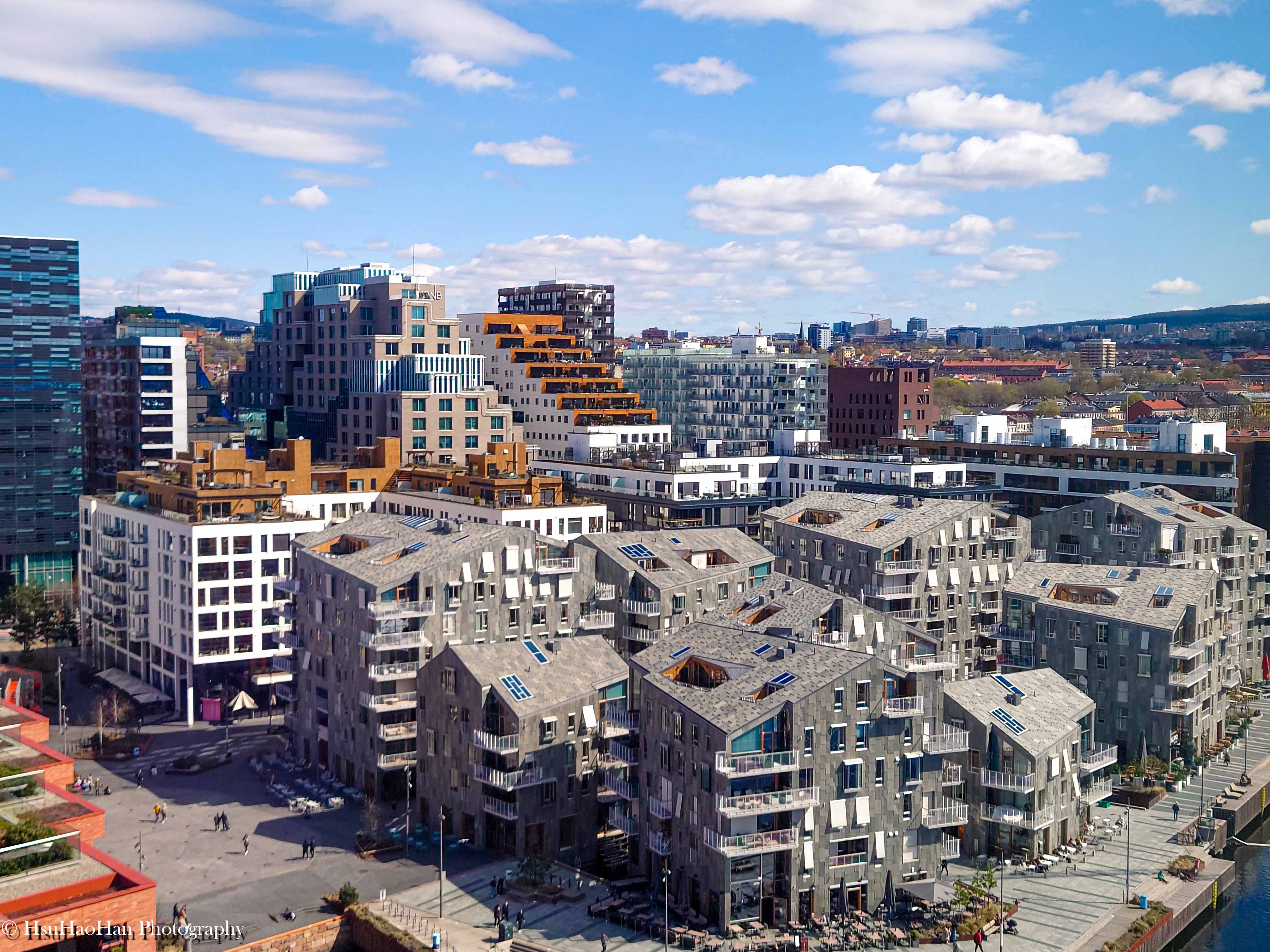 挪威奧斯陸Sørenga住宅區的建築群，有著不規則的石材立面與退縮的陽台，遠方背景是「條碼計畫」的現代建築。