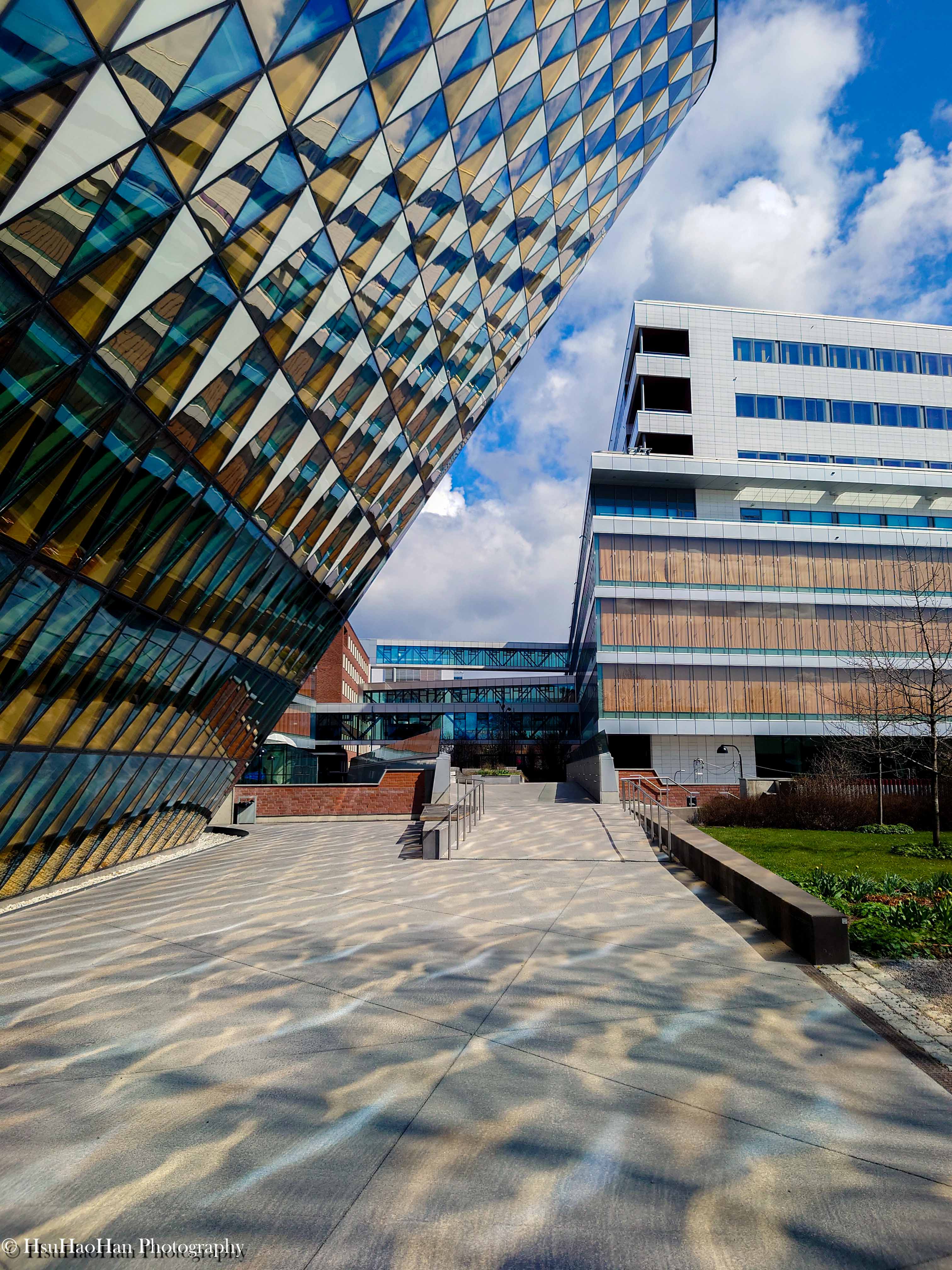 從低角度仰望瑞典斯德哥爾摩的 Aula Medica 建築，由無數三角玻璃構成的巨大曲面，在藍天白雲下顯得氣勢恢宏。