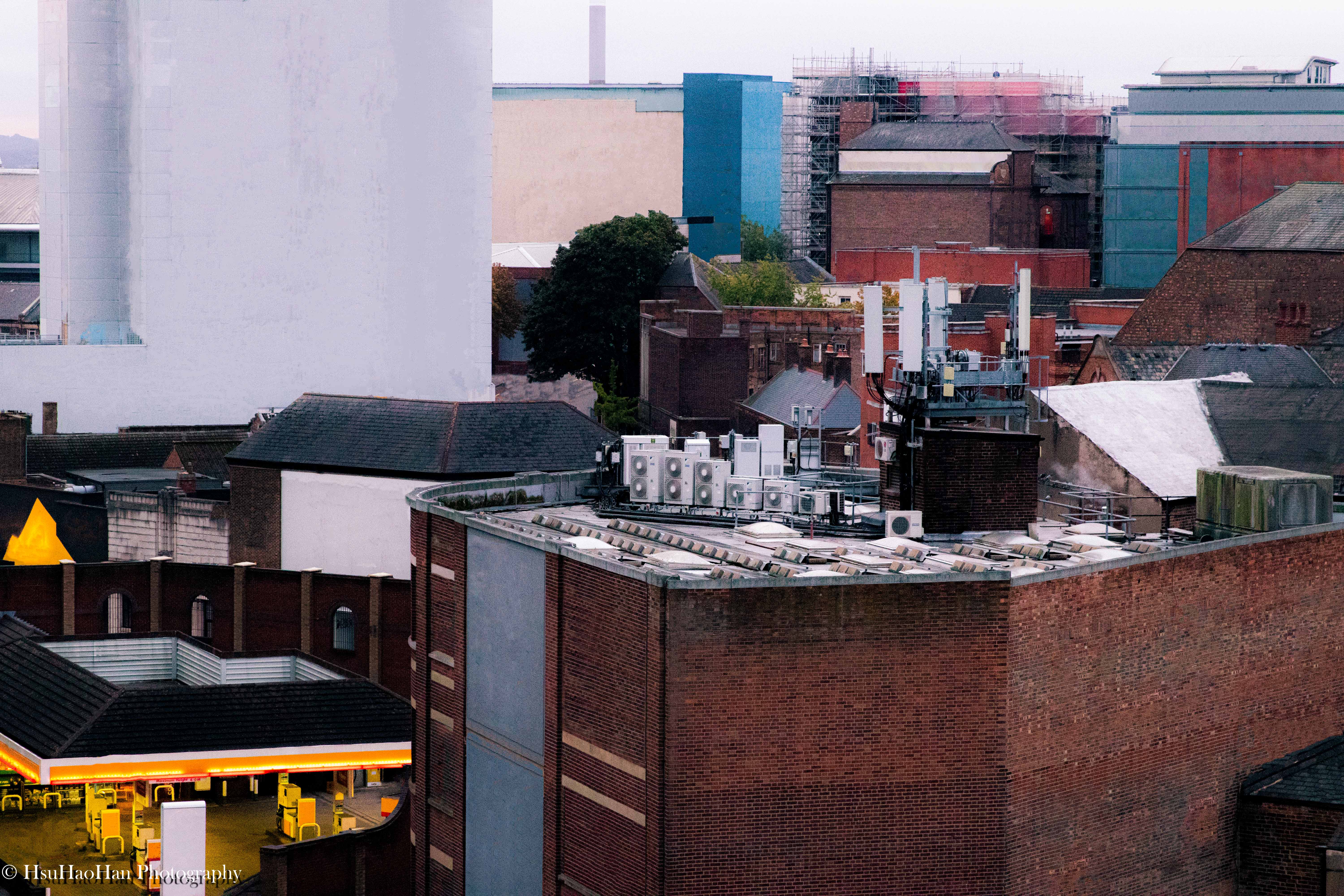 徐浩瀚「城市再現」系列:英國諾丁漢的城市天際線,前景為紅磚屋頂與空調設備,遠景可見不同材質與色彩的新舊建築群。