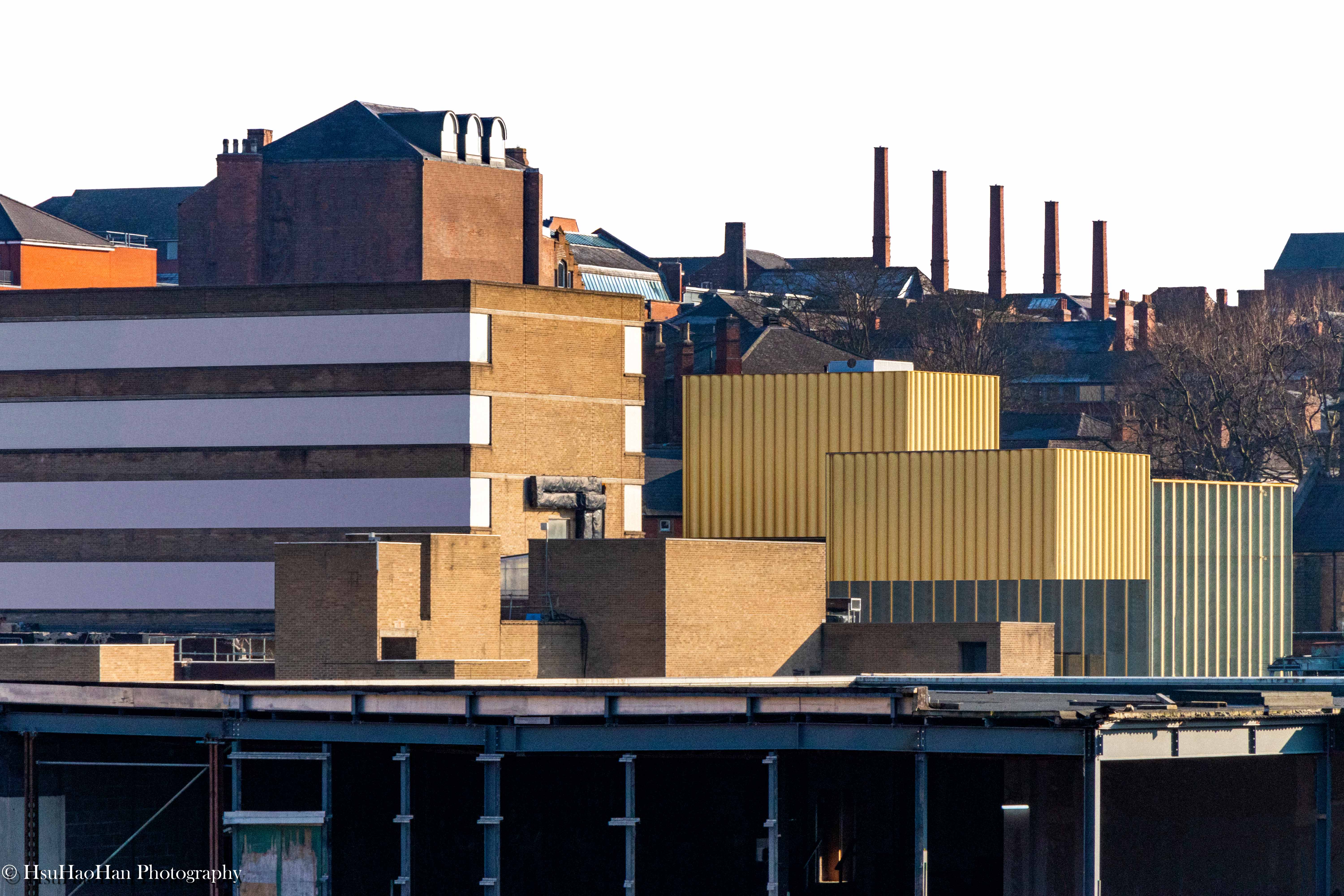 徐浩瀚「城市再現」系列:英國諾丁漢的城市天際線,前景為紅磚屋頂與空調設備,遠景可見不同材質與色彩的新舊建築群。