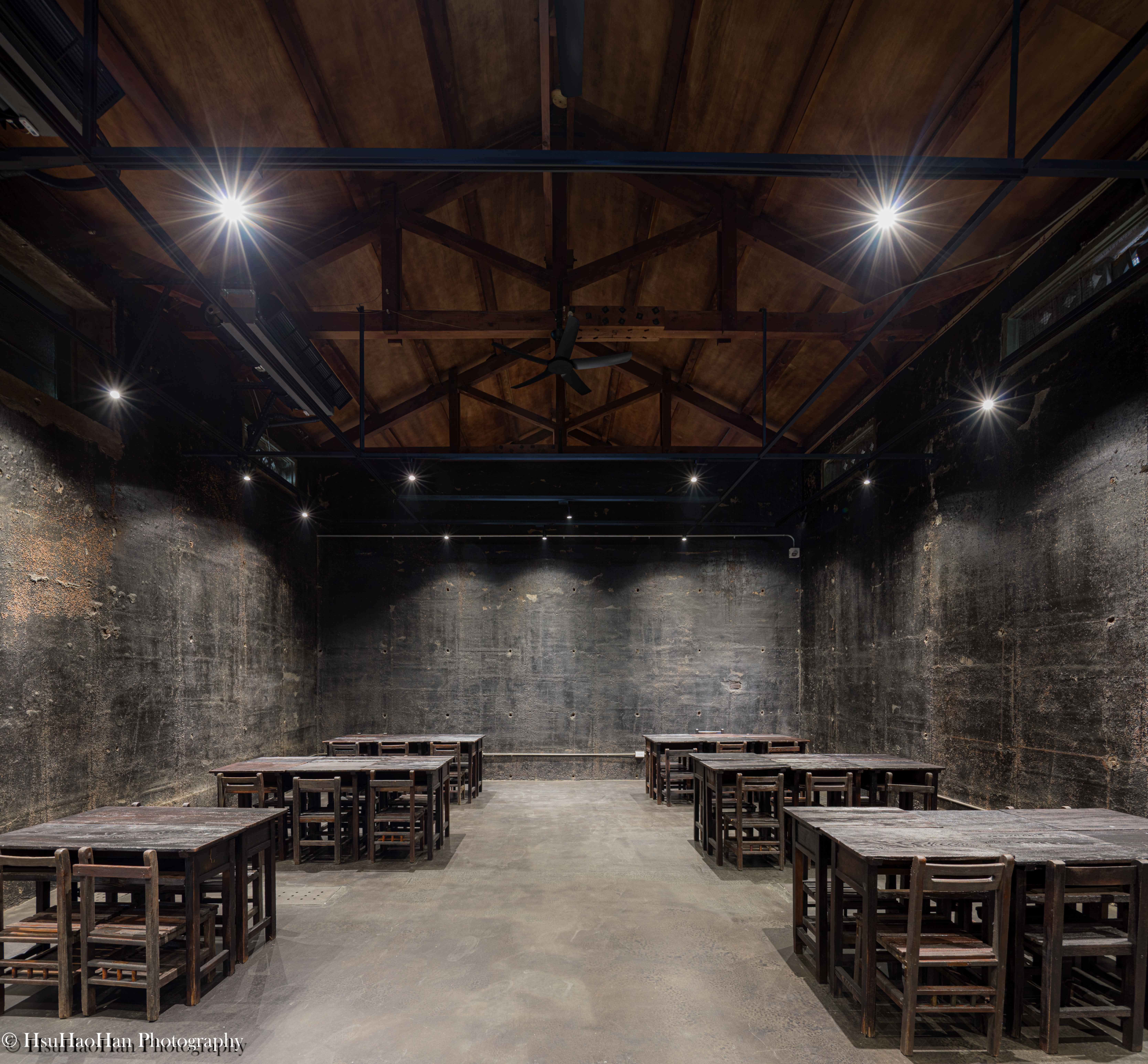Renovated interior of "Winter Storage Pavilion" featuring original wooden roof trusses and dark textured walls - 國姓鄉農會冬藏雅閣舊穀倉改建休憩區保留原有木造桁架與深色牆面氛圍 - Photography by Hsu Hao Han