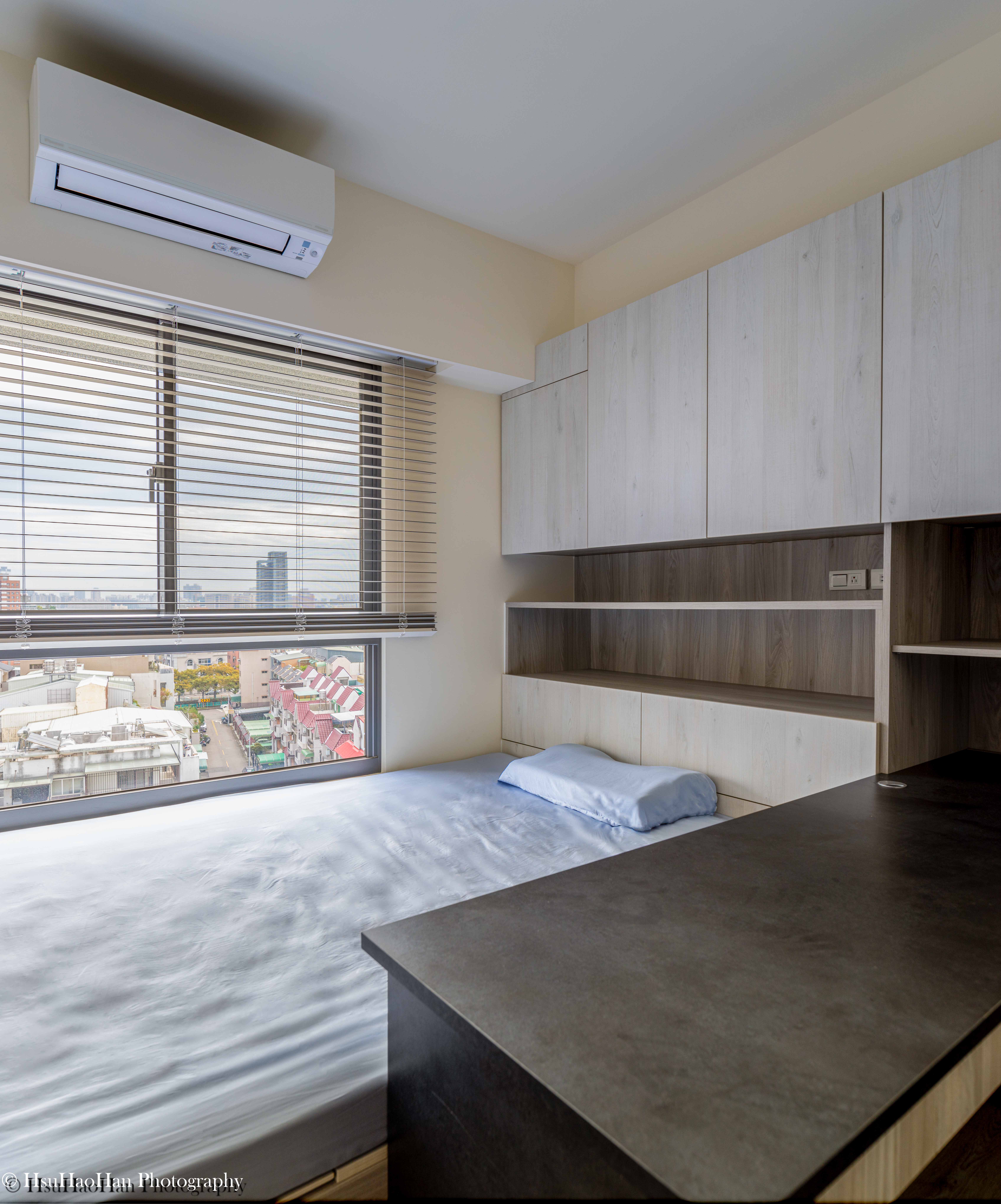 台中「黎民觀邸」的次臥室，採用架高的木質地板與臥榻設計，書桌與床鋪及收納櫃體整合在一起，空間利用極大化。