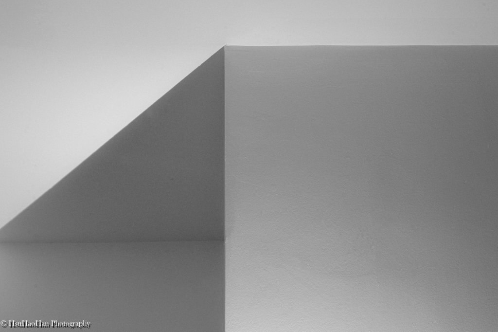 徐浩瀚「平面空間」系列中的黑白抽象攝影，房間角落的光影在牆面上，形成簡潔的幾何線條與柔和的漸層。