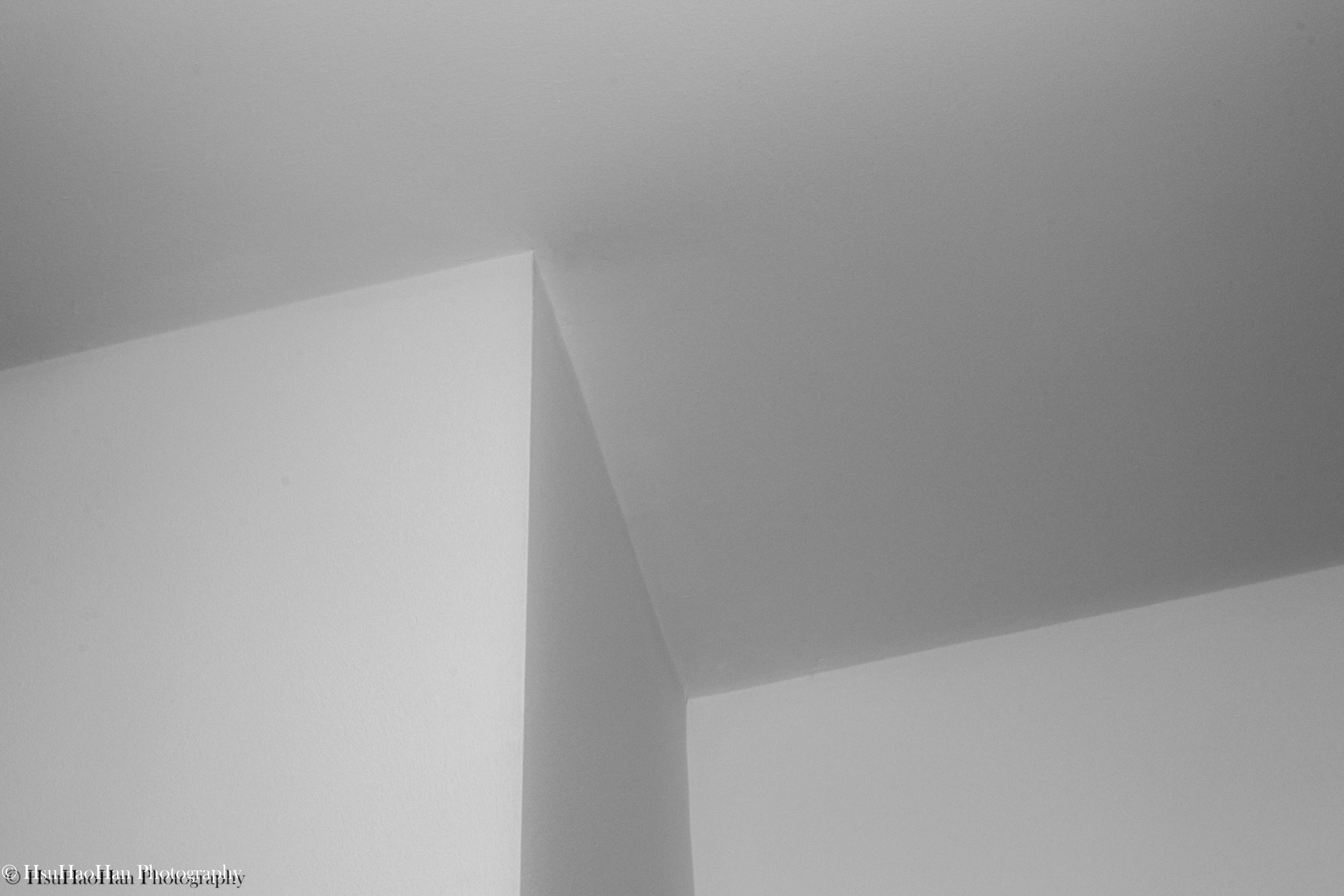 徐浩瀚「平面空間」系列中的黑白抽象攝影，房間角落的光影在牆面上，形成簡潔的幾何線條與柔和的漸層。