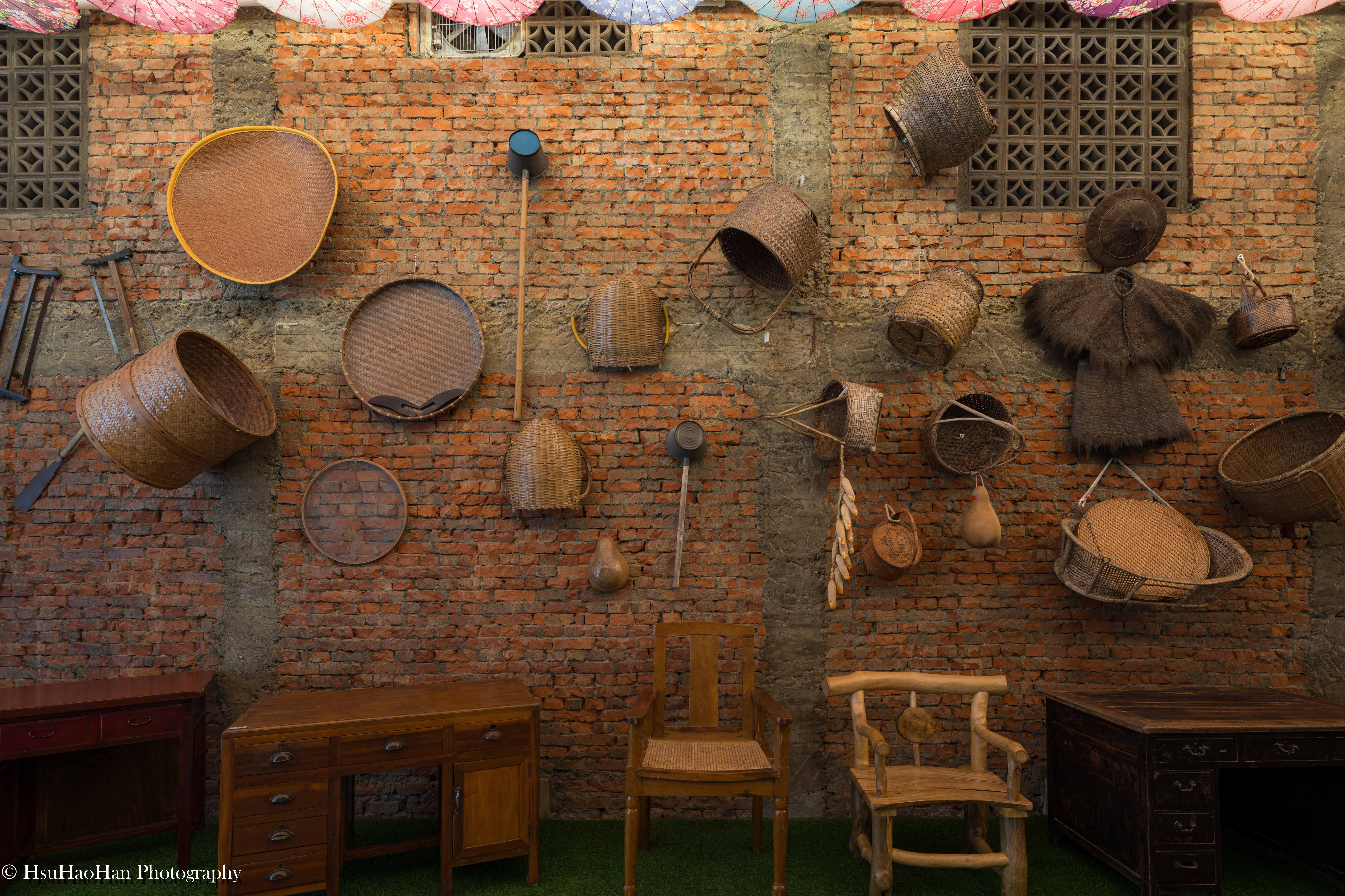 Traditional bamboo baskets and vintage farming equipment displayed on a historic red brick wall - 傳統竹編籃筐與農耕器具掛飾於斑駁紅磚牆面的文化展示 - Photography by Hsu Hao Han