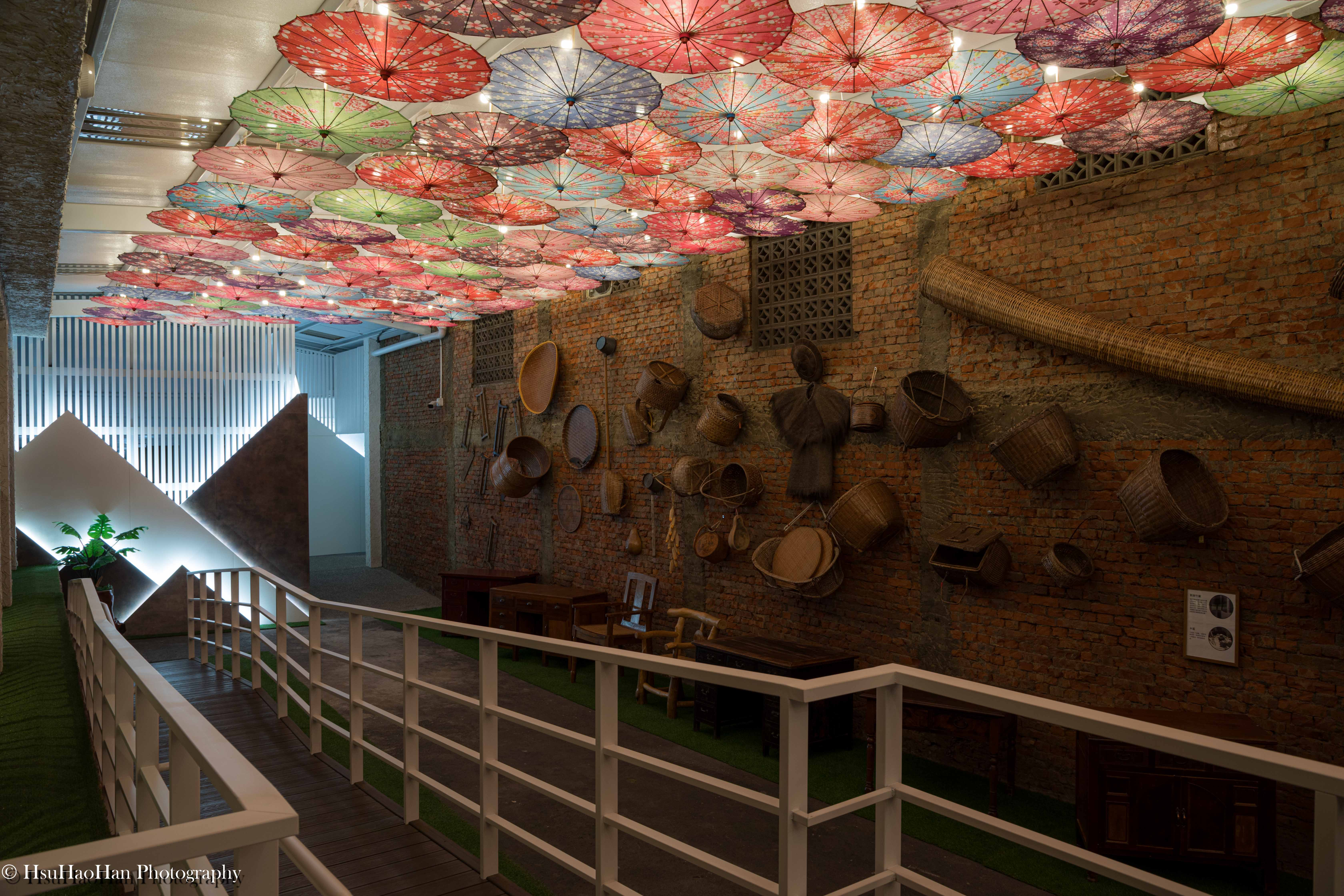 Colorful paper umbrellas ceiling installation and red brick wall displaying farming tools at Xiayun Corridor - 國姓鄉農會文創園區夏耘廊道客家紙傘裝置藝術與紅磚牆農具展示 - Photography by Hsu Hao Han