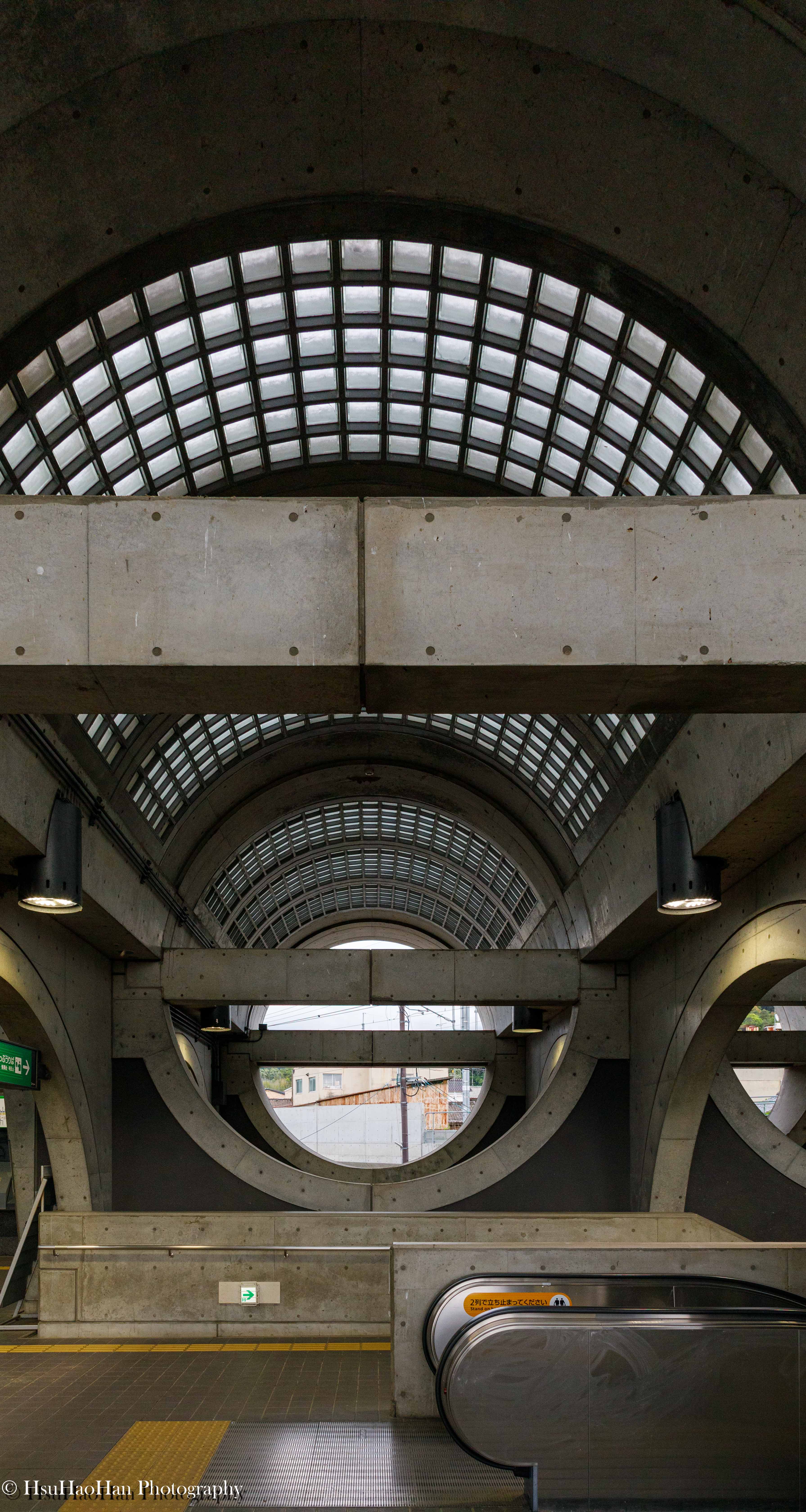 若林広幸設計的宇治車站內部大廳，巨大的圓拱形玻璃磚天窗，與粗獷的清水混凝土樑柱構成對稱而充滿力量感的空間。