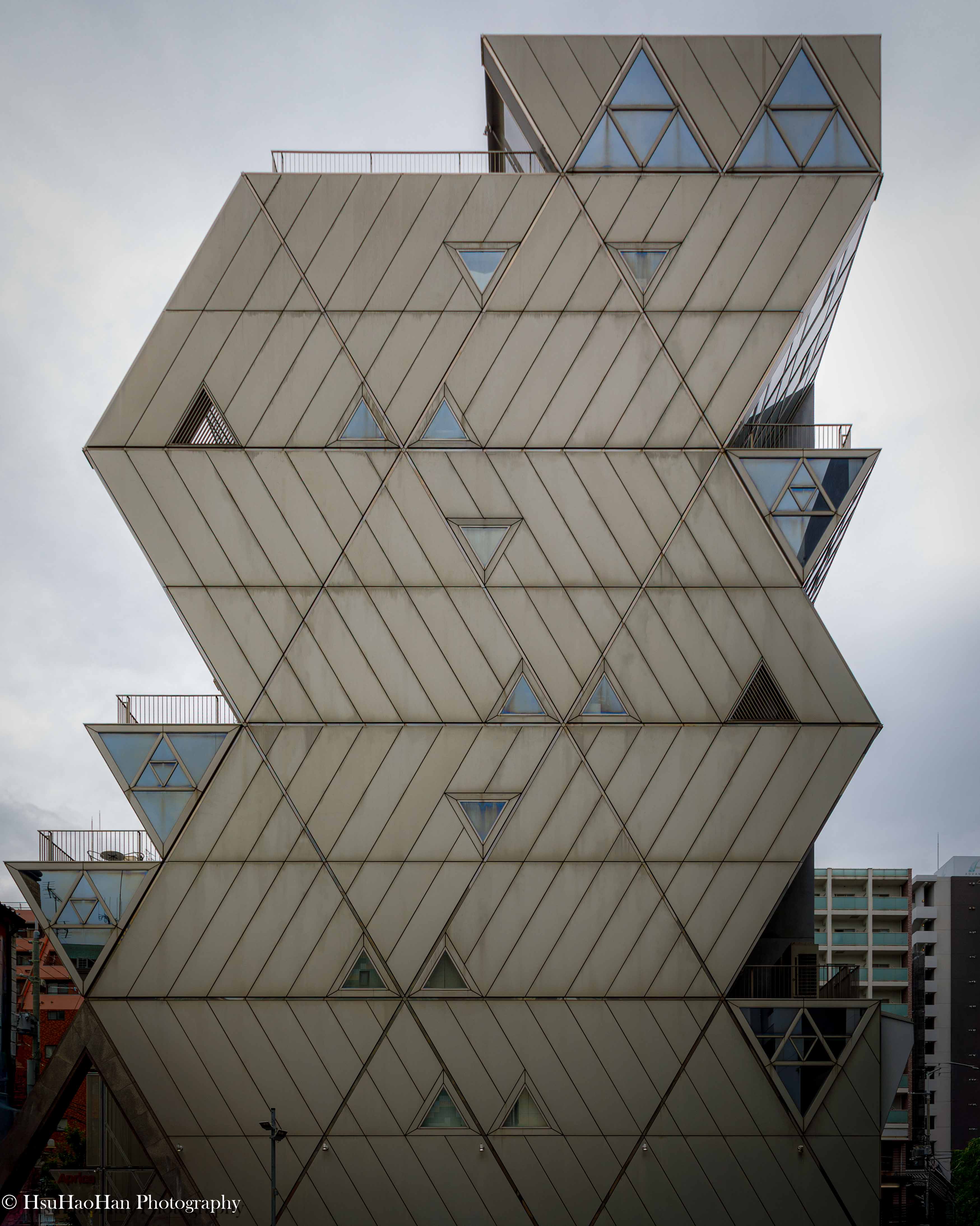由建築大師丹下健三設計的日本大阪 Aprica Kasai 總部大樓，建築外觀呈現為鋸齒狀堆疊的金屬板塊，點綴著三角形的窗戶。