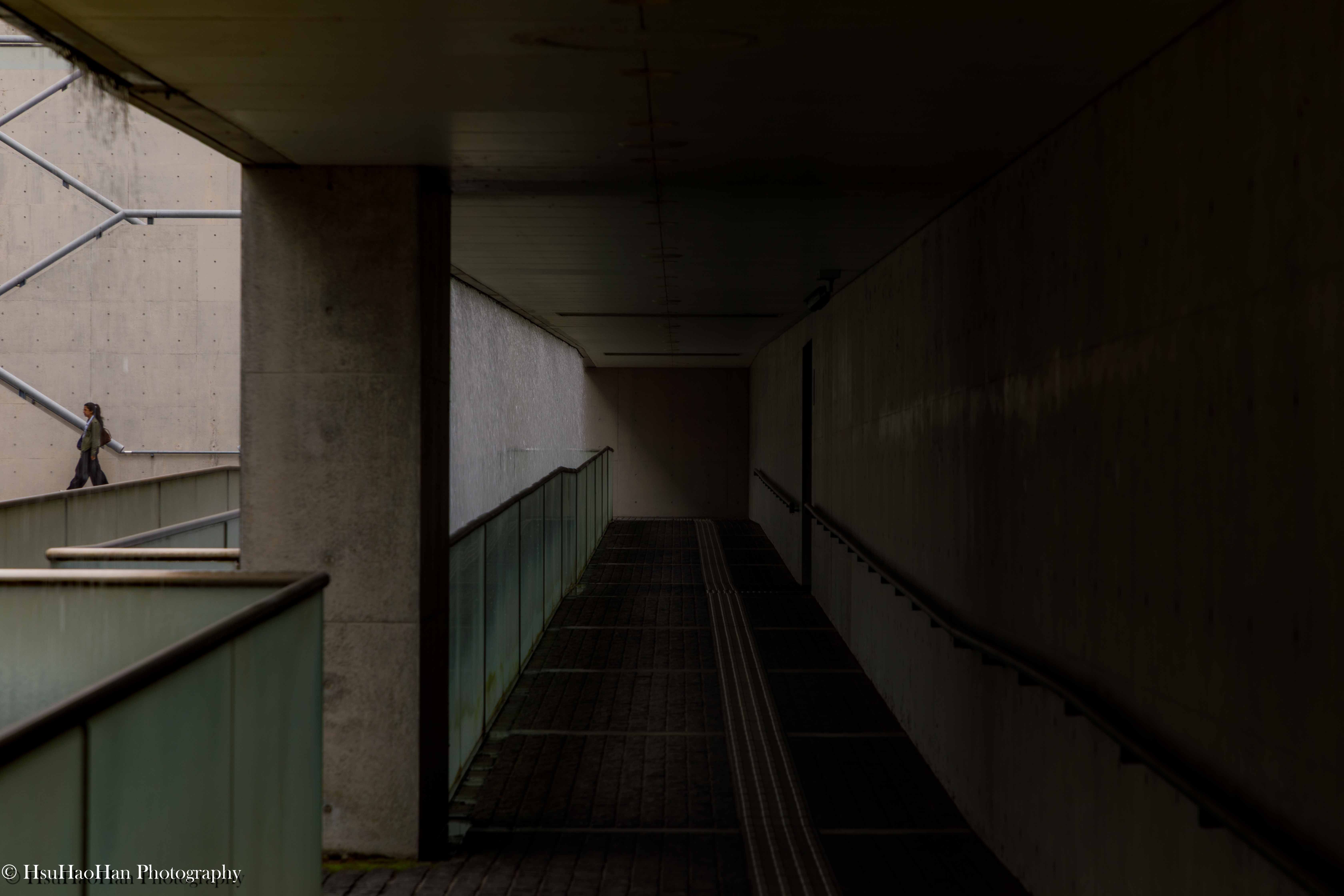 狹山池博物館內部的清水混凝土坡道，一位訪客的身影沿著斜坡行走，明暗光影對比強烈，充滿空間感。